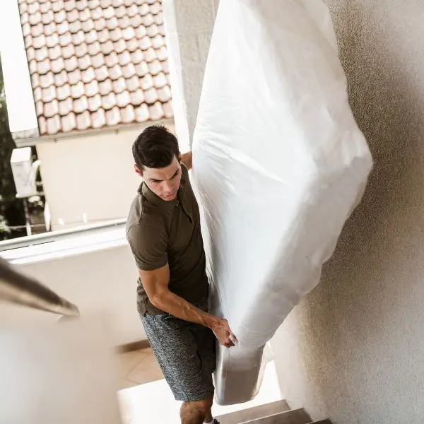 homme qui monte un matelas dans des escaliers